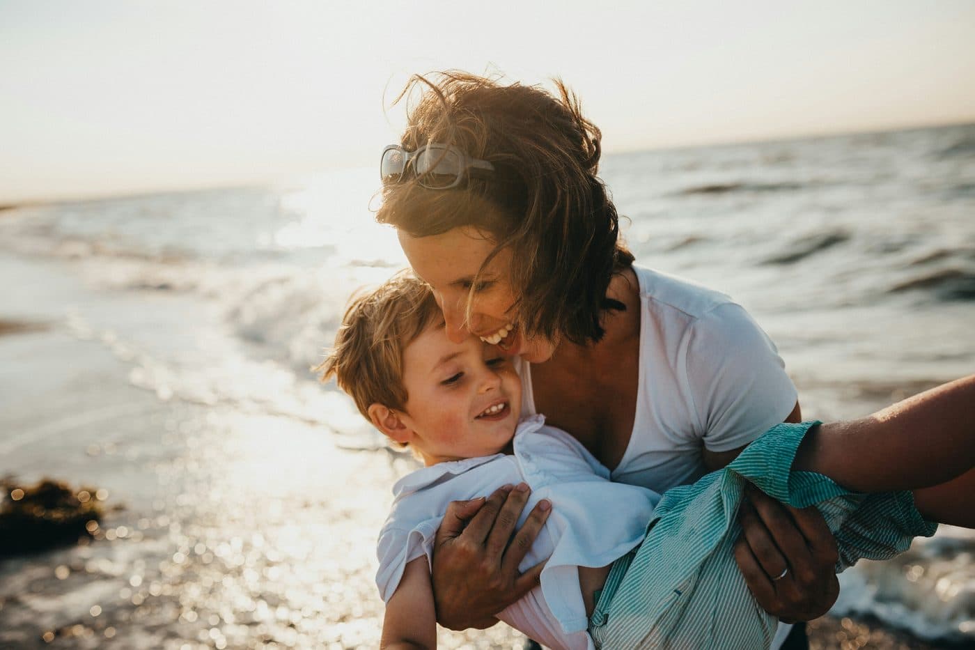 Mãe abraçando o filho na praia ao entardecer